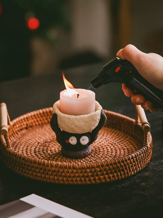 Hand lighting a pillar candle in a handmade ceramic figure candle holder set on a round woven tray.