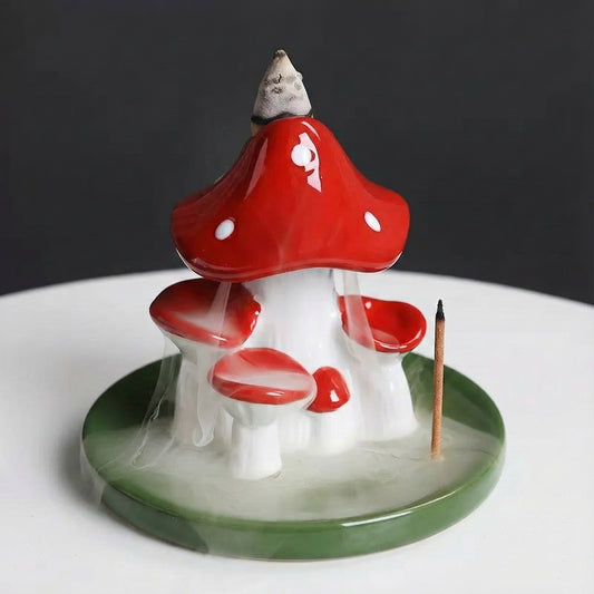 Red and white ceramic mushroom backflow incense burner on a green leaf base showing smoke waterfall effect and a stick incense holder