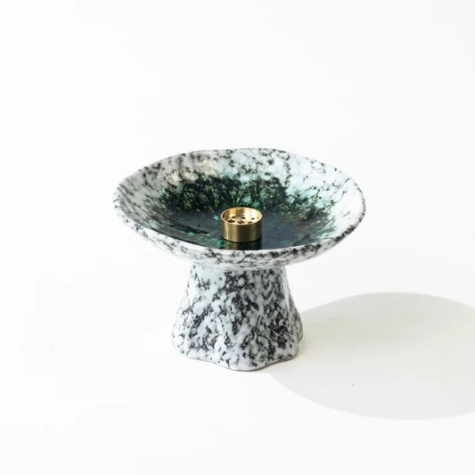 Handmade Japanese wabi-sabi style pedestal ceramic incense holder with white and black speckled glaze and deep green center, featuring a brass incense insert on a white background.
