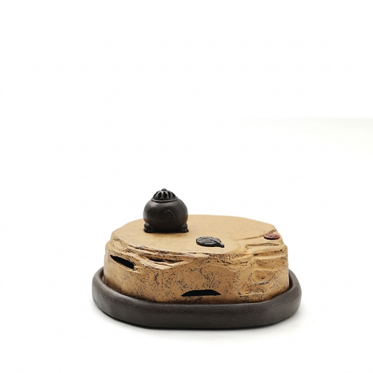 Handmade Yixing purple clay incense burner with a low round profile, textured tan lid, small black vented dome top, and dark circular base, shown against a white background.