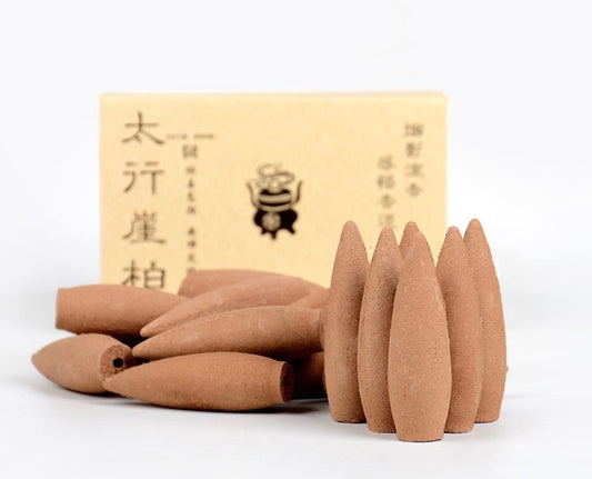 Longer burn thuja backflow incense cones in elongated bullet shape stacked beside a paper card for use with backflow incense burners