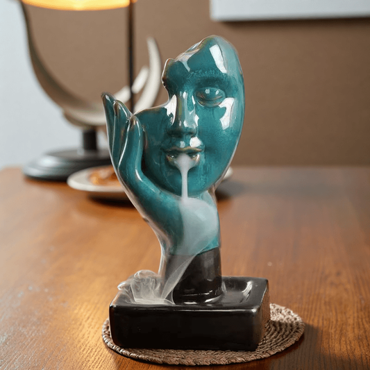 Front view of Abstract Face Backflow Incense Burner with turquoise glaze and flowing smoke.