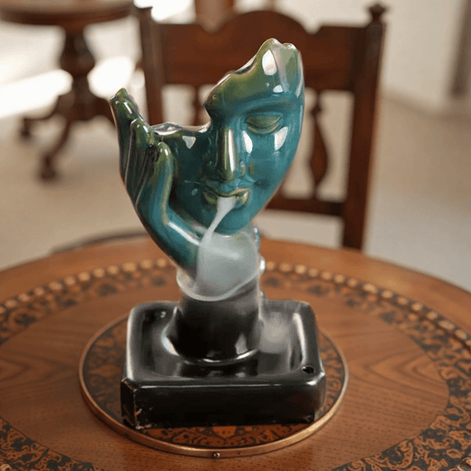 Close-up of Abstract Face Backflow Incense Burner with smoke streaming from mouth on carved wooden table.