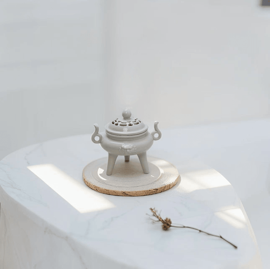 Antique-style three-legged ceramic incense burner displayed on wooden tray with natural light, styled for home decor or meditation space