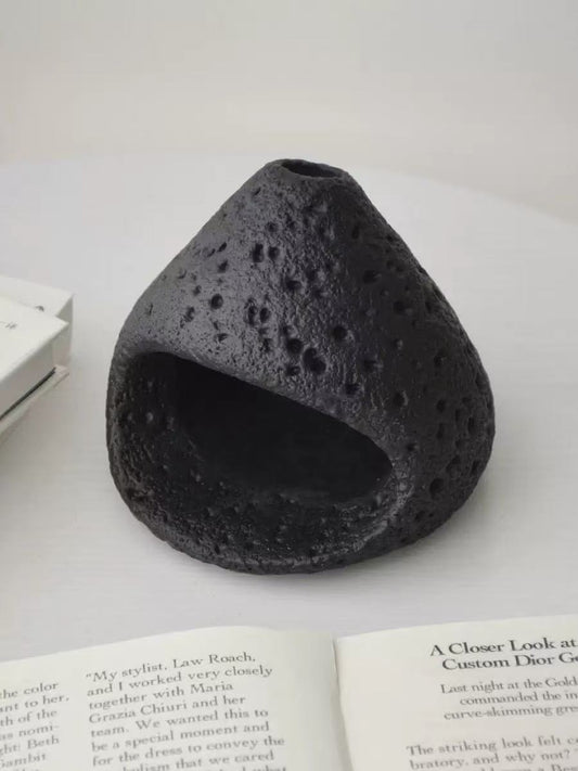 Natural black stone incense burner with a volcanic texture, displayed on an open book and white surface in a minimalist setting