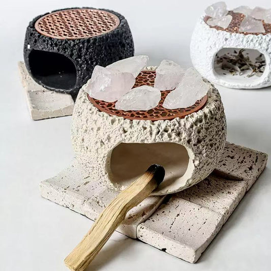 Handmade cement crystal purifier stoves in black, white, and off-white colors, with rosewood grates and raw crystals on top, shown with a lit palo santo stick on a minimalist white background