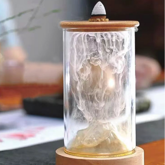 Glass backflow incense burner with wooden base and lid, showing volcano-shaped smoke effect flowing down inside the cylinder.