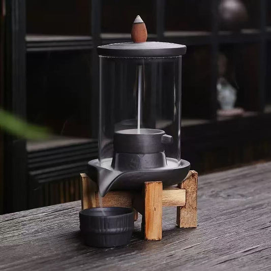 Backflow incense burner with a transparent glass cylinder, metal base, and wooden stand, placed on a rustic wooden surface.