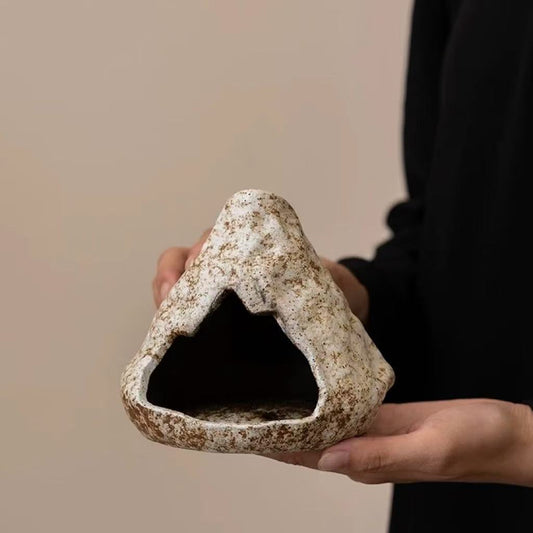 Hand holding a handmade ceramic incense burner with natural stone texture, showing the hollow triangular front opening against a beige background