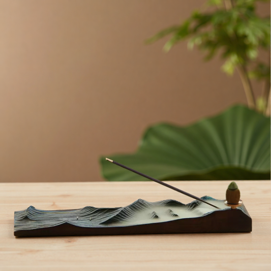 Mountain Mist Incense Holder with incense stick and backflow cone placed on wooden surface, styled with a large green leaf in the background