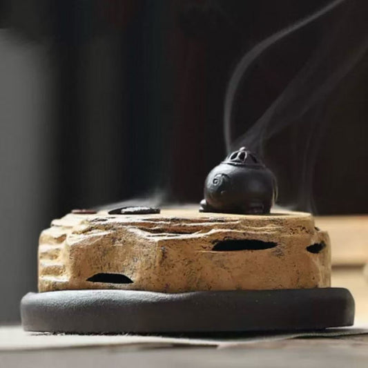Handmade vintage-style purple clay incense burner with smoke flowing from the lid on a wooden base