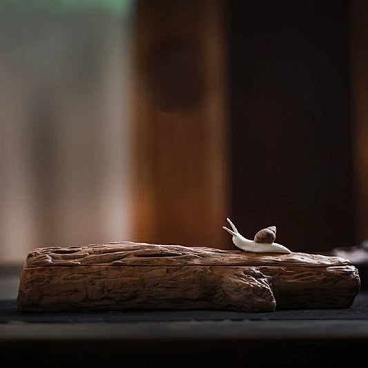 Snail-shaped handmade incense holder resting on a rustic wooden base, against a warm dim background