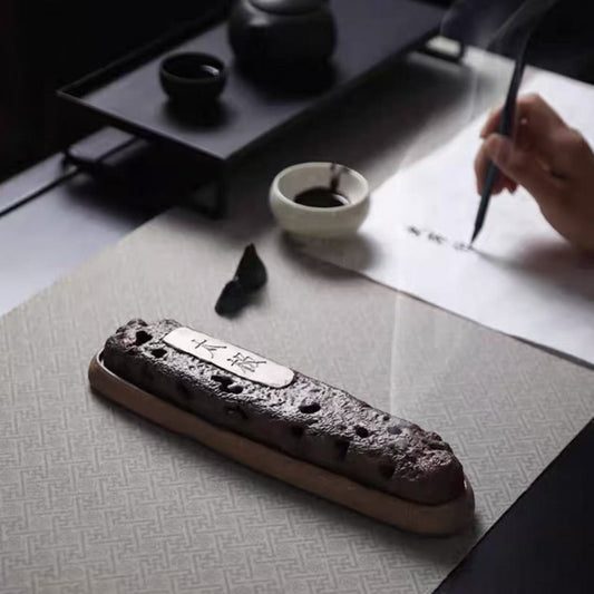 Rustic volcanic ceramic incense holder placed next to calligraphy tools and handwritten script in a traditional setting