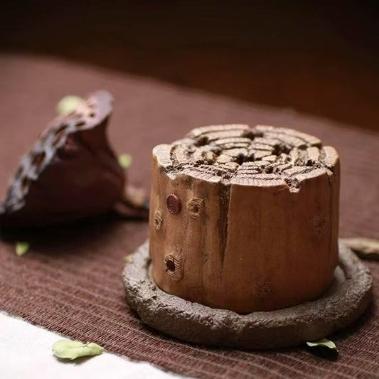 Side view of a hand-carved wood-stump style incense burner with coiled incense on top, placed on a rustic brown fabric
