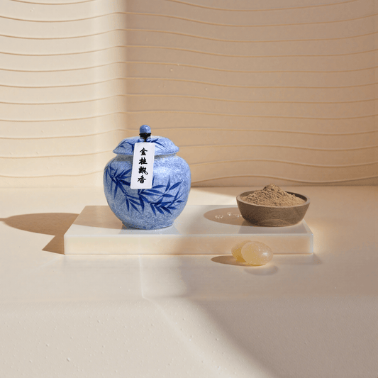Golden Osmanthus incense powder in a blue ceramic jar placed beside a wooden bowl used to display the incense powder