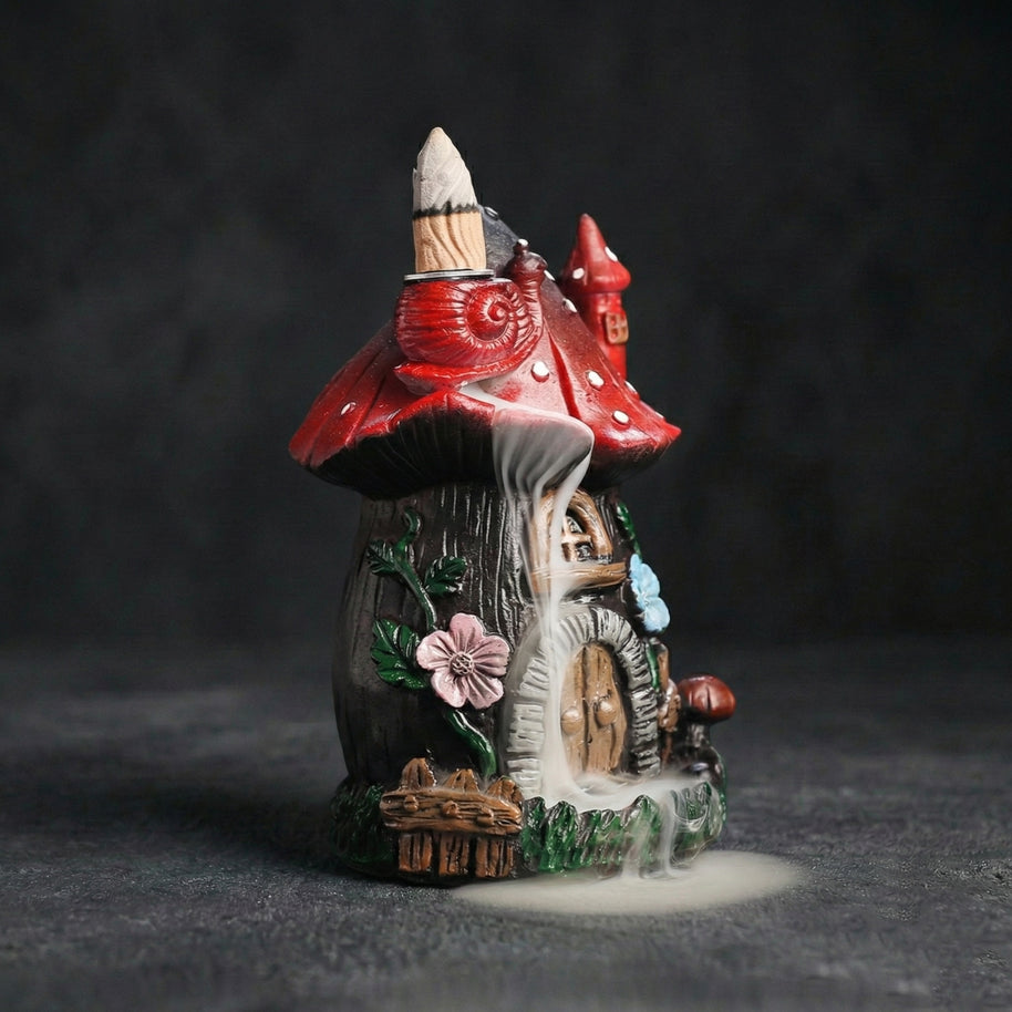 Side view of the resin mushroom backflow incense burner in action, showcasing the mesmerizing smoke waterfall effect cascading down the fairy house details, including a red snail, floral accents, and a rustic door. Ideal for cottagecore room decor and aromatherapy.