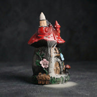 Side view of the resin mushroom backflow incense burner in action, showcasing the mesmerizing smoke waterfall effect cascading down the fairy house details, including a red snail, floral accents, and a rustic door. Ideal for cottagecore room decor and aromatherapy.