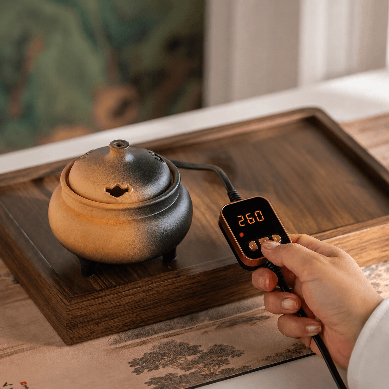 Hand adjusting the temperature controller of a ceramic electric incense burner to 260°C for precise flameless incense heating.