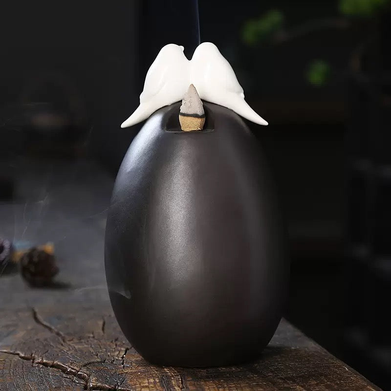Rear view of the Backflow Incense Burner Ceramic Waterfall with Doves, showing the smooth black ceramic body, dove topper, and incense cone placement on a rustic wooden surface