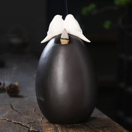 Rear view of the Backflow Incense Burner Ceramic Waterfall with Doves, showing the smooth black ceramic body, dove topper, and incense cone placement on a rustic wooden surface
