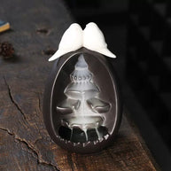 Backflow Incense Burner Ceramic Waterfall with Doves shown in use on a wooden surface, featuring cascading incense smoke flowing down the tiered ceramic waterfall beneath two white doves on top