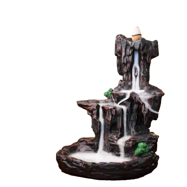 Mountain waterfall-style backflow incense burner with layered dark rock terraces, a cone holder at the top, and white cascading smoke flowing down into the basin below.