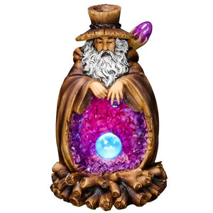 Resin wizard incense burner with a long white beard, brown cloak, purple crystal-like center, and a glowing blue crystal ball set above a wood-style base on a light background.
