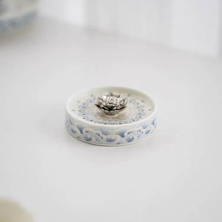 Angled view of a blue and white ceramic incense holder with a raised silver lotus centerpiece and decorative floral pattern