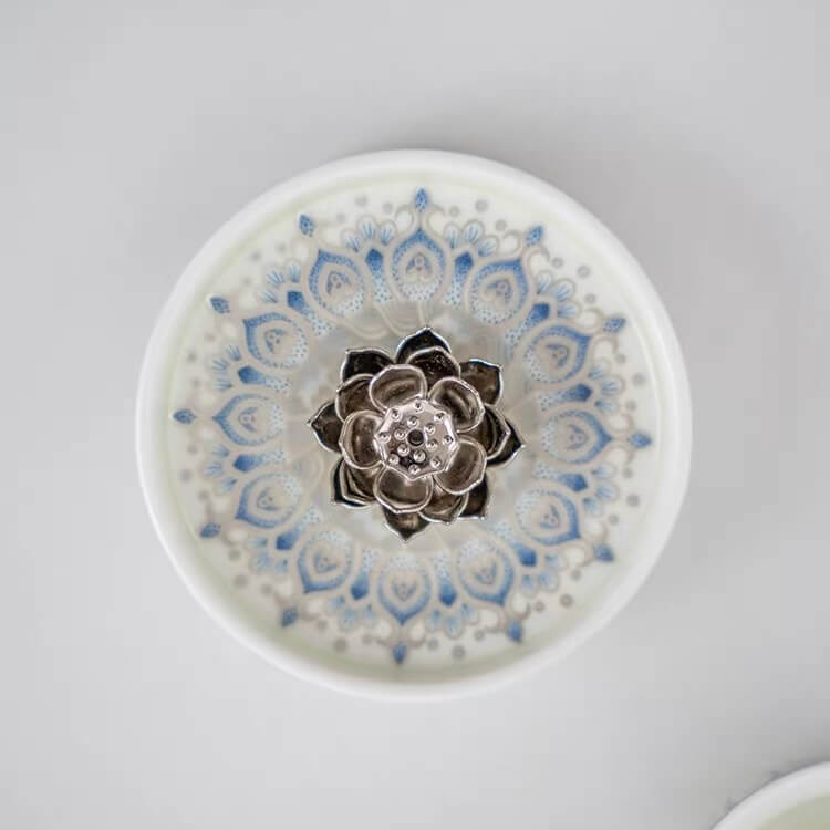 Top view of a blue and white ceramic incense holder with a raised silver lotus centerpiece and circular floral pattern