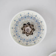 Top view of a blue and white ceramic incense holder with a raised silver lotus centerpiece and circular floral pattern