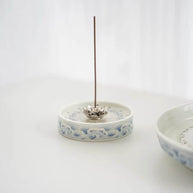 Blue and white ceramic lotus incense holder holding a single upright incense stick on a white background