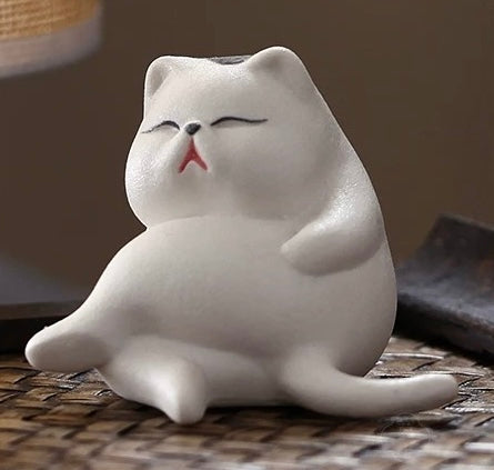 White ceramic cat incense holder in a relaxed sitting pose on a woven surface, front angle, no incense stick inserted.