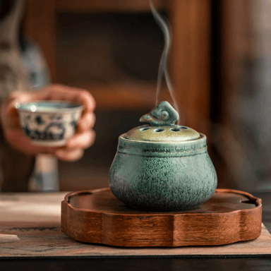 ceramic electric incense burner on a wooden tray, releasing gentle aroma smoke for a calm tea room, meditation, or home fragrance setting.