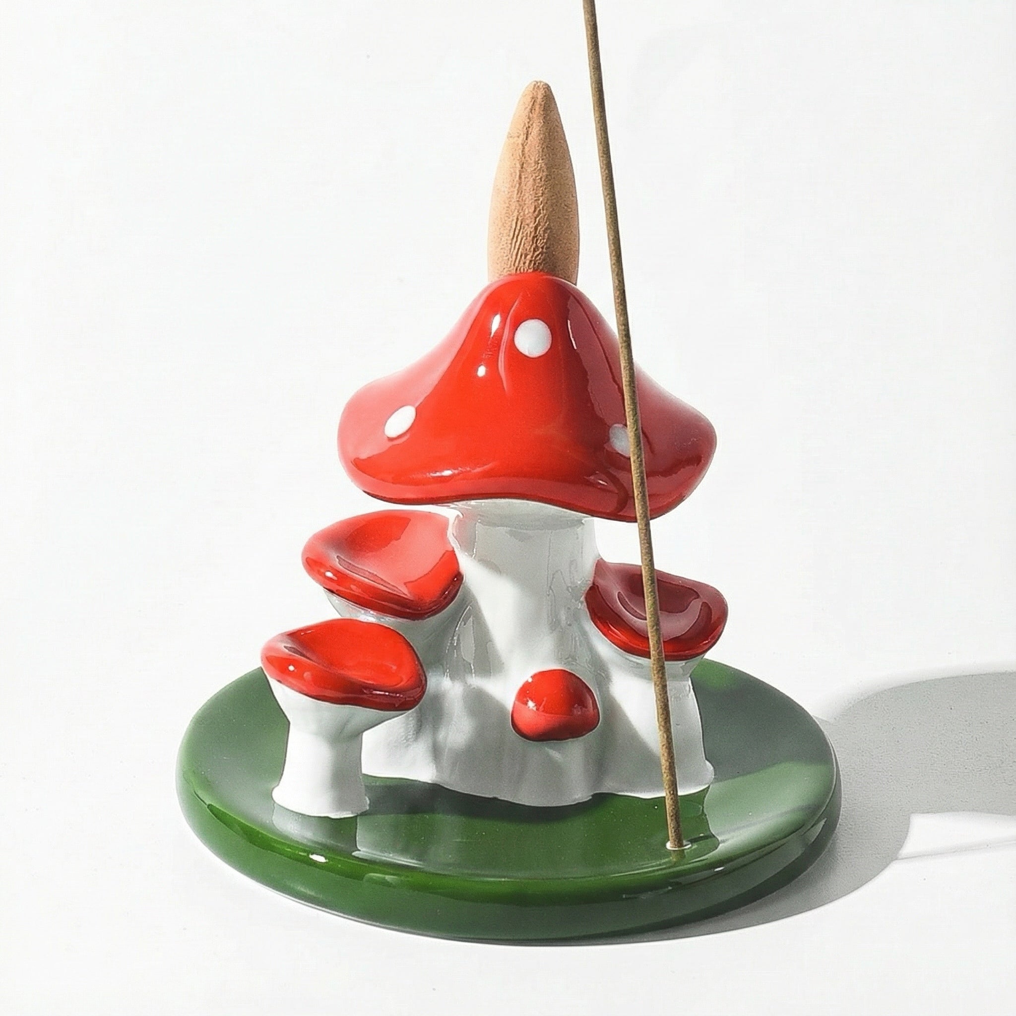 Ceramic mushroom backflow incense burner with a stick holder, featuring glossy red mushroom caps with white dots, white mushroom stems, and a green leaf-shaped base for cone and stick incense.