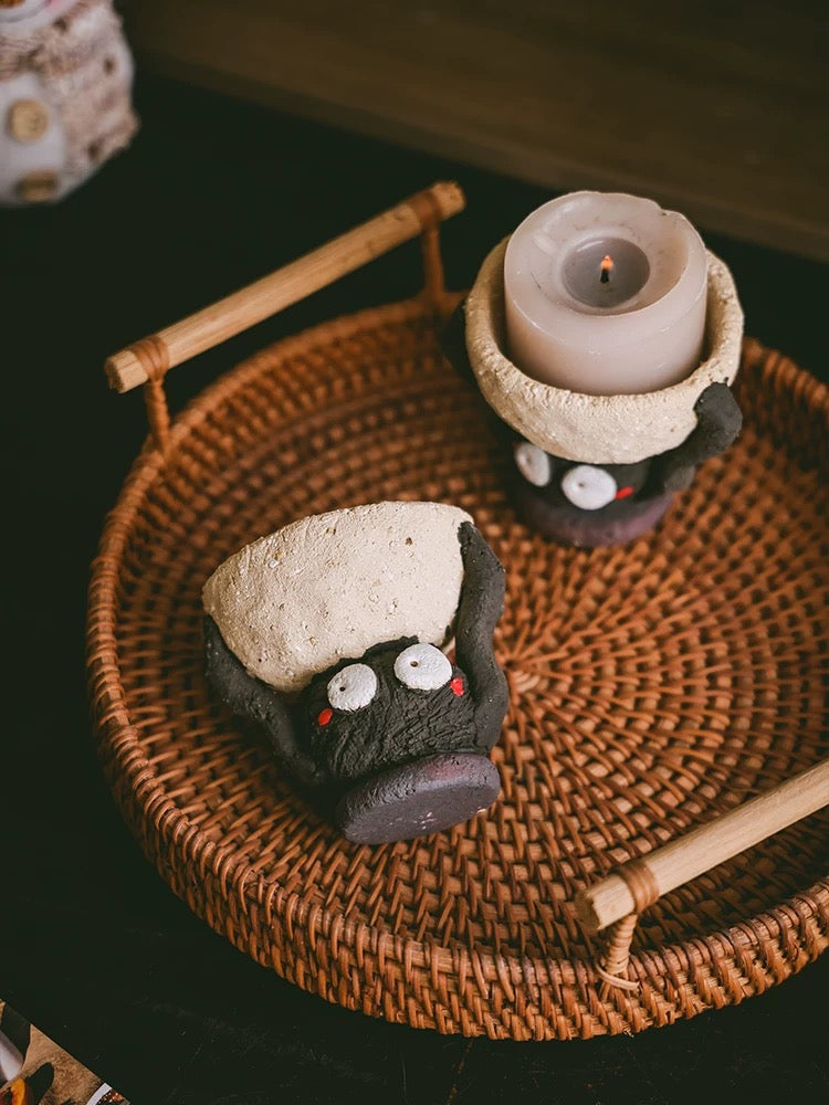 Handmade ceramic Soot Spirit candle holders displayed on a woven tray, with one holding a lit tealight candle.
