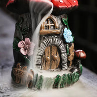 Close-up base details of the resin mushroom backflow incense burner, showing the mesmerizing thick smoke waterfall cascading down past a miniature fairy door, rustic stone textures, and vibrant pink and blue flower accents. Perfect for cottagecore room decor and aromatherapy.