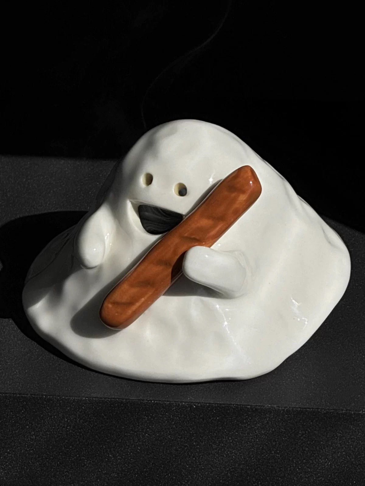 Hand-painted ceramic ghost incense holder for cone incense in glossy white, dramatic lighting on a dark stone shelf.