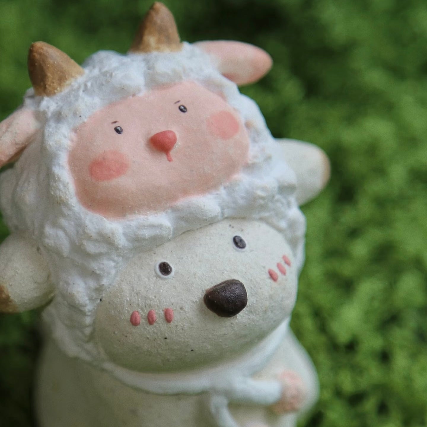 Close-up detail of a custom handmade ceramic incense holder featuring a cute bear in a fluffy sheep costume against a green moss background