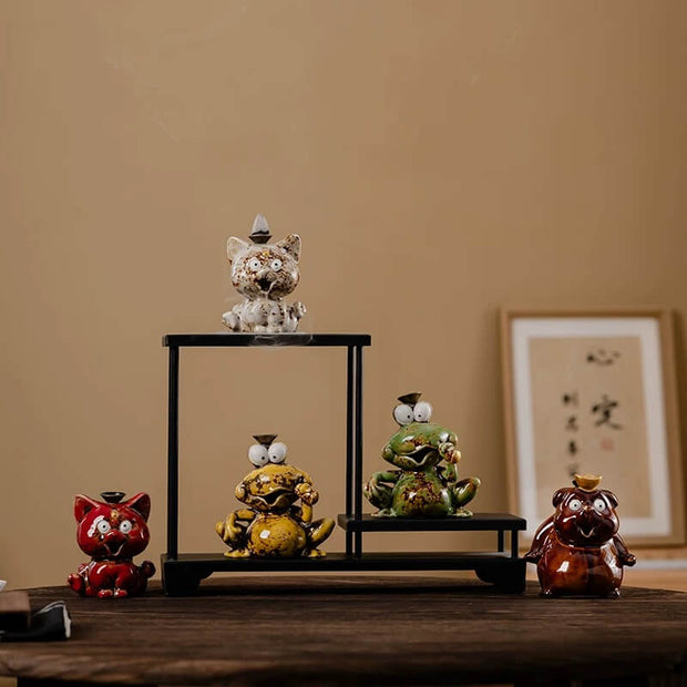 A collection of five glossy ceramic cute animal backflow incense burners in various colors like green, yellow, red, and white, arranged on and around a small black display stand on a wooden table.