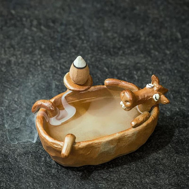Cute brown animal relaxing in a small bathtub shaped backflow incense burner with a cone creating a flowing smoke effect