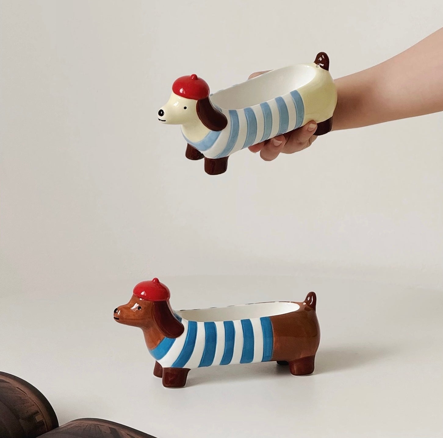 Light blue dachshund incense holder held in hand above a brown striped version on a white backdrop for size reference.