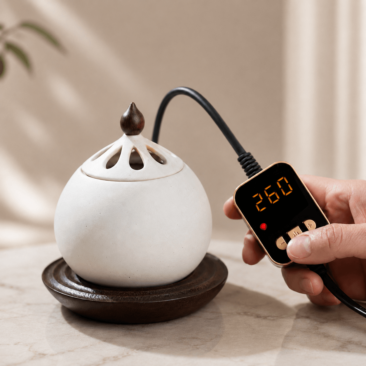 A hand adjusting the digital temperature controller displaying 260°C for a white electric ceramic incense burner sitting on a solid wood base