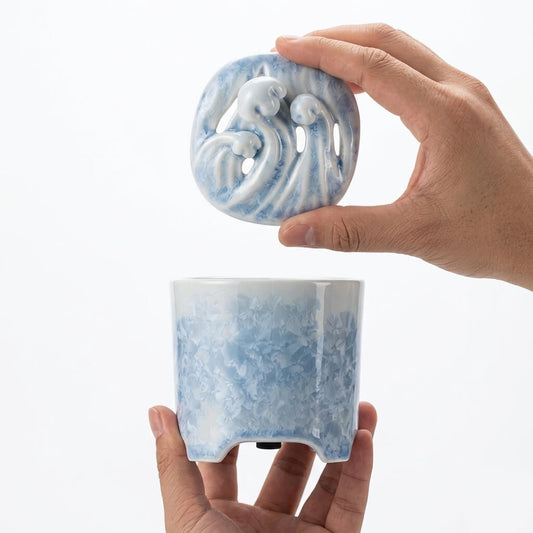 Hand holding a blue and white crystalline glaze ceramic electric incense burner with a removable vented lid.
