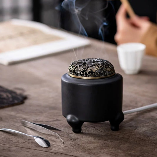 Electric incense burner with digital adjustable temperature and timer, shown in use on a tabletop with rising incense smoke, tweezers, and spoon in a warm tea setting