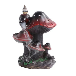 Front view of a creative resin backflow incense burner featuring a whimsical cluster of dark red and black mushrooms with white spots. A lit incense cone rests on top, creating a mesmerizing and soothing smoke waterfall effect that cascades down the mushroom caps to a rocky, moss-accented base. Perfect for unique nature-inspired room decor and relaxing aromatherapy.