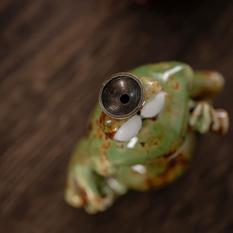A top-down close-up view of a green speckled ceramic frog backflow incense burner, focusing on the metal holder on top of its head where the incense cone is placed.