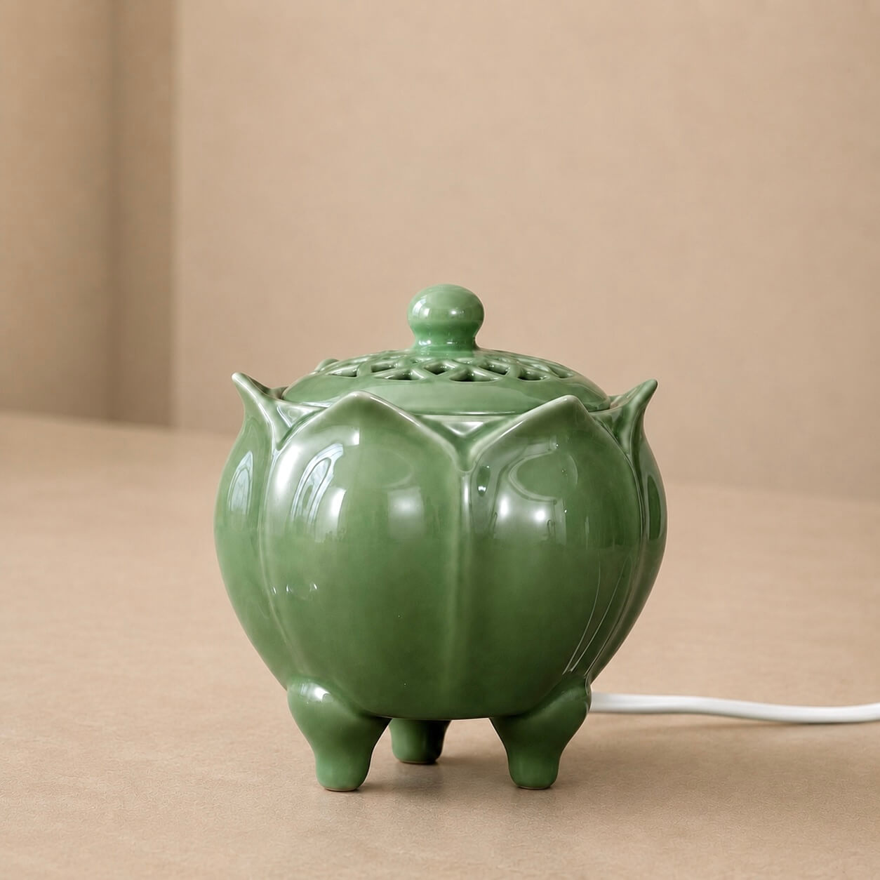 Glossy green lotus shaped electric incense burner with a vented lid and power cord displayed on a beige surface