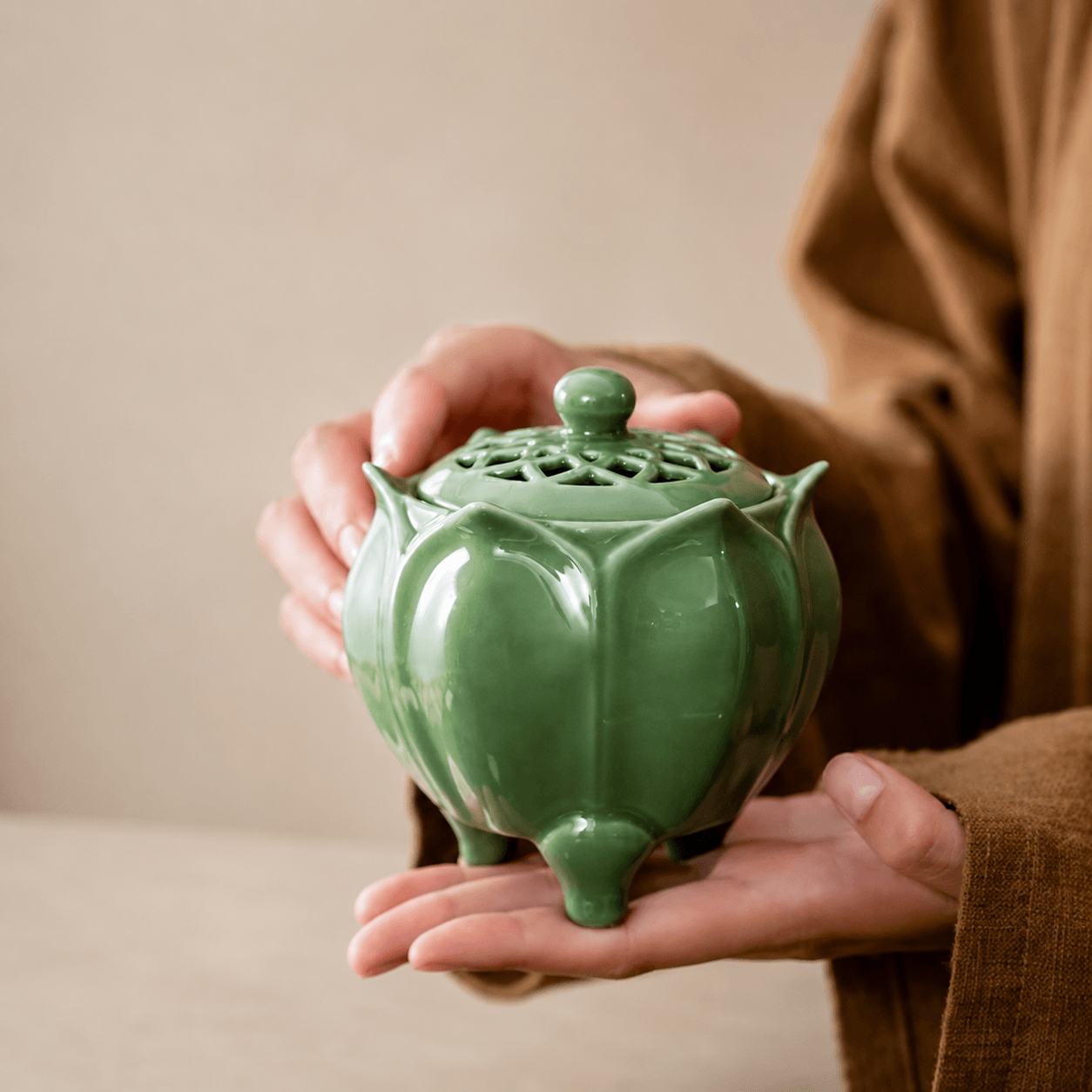 Person holding a glossy green lotus shaped electric incense burner with a decorative vented lid