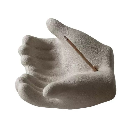 Front view of a hand-shaped ceramic incense holder with a minimalist zen design, featuring a textured cupped palm and a single incense stick resting diagonally across the hand on a clean white background.