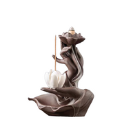 Sculptural incense burner featuring a dark hand-shaped base and flowing branch-like form, with a lotus flower at the top holding a backflow cone, a white lotus below, and a vertical incense stick suspended beside it against a white background.